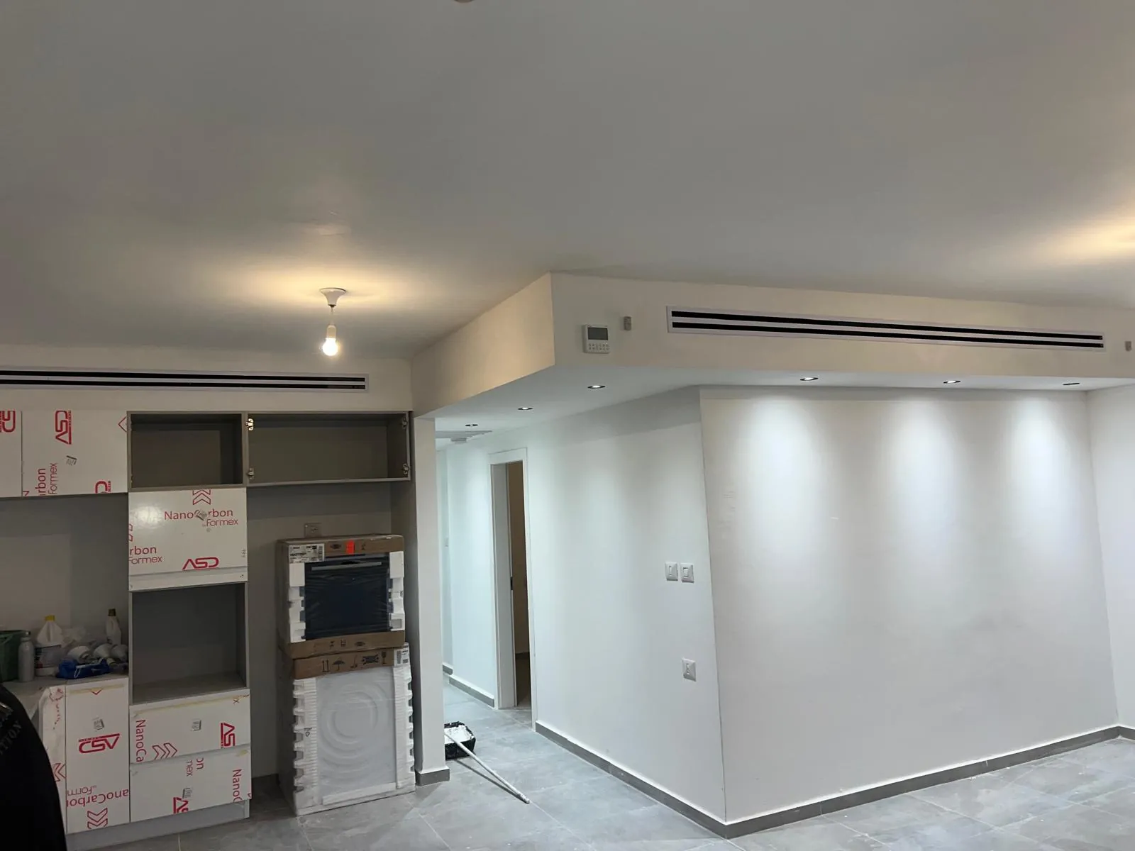 תיבת גבס עם תעלת אוויר ליניארית מעל מטבח בשיפוץ עם ארונות עדיין סגורים באריזה